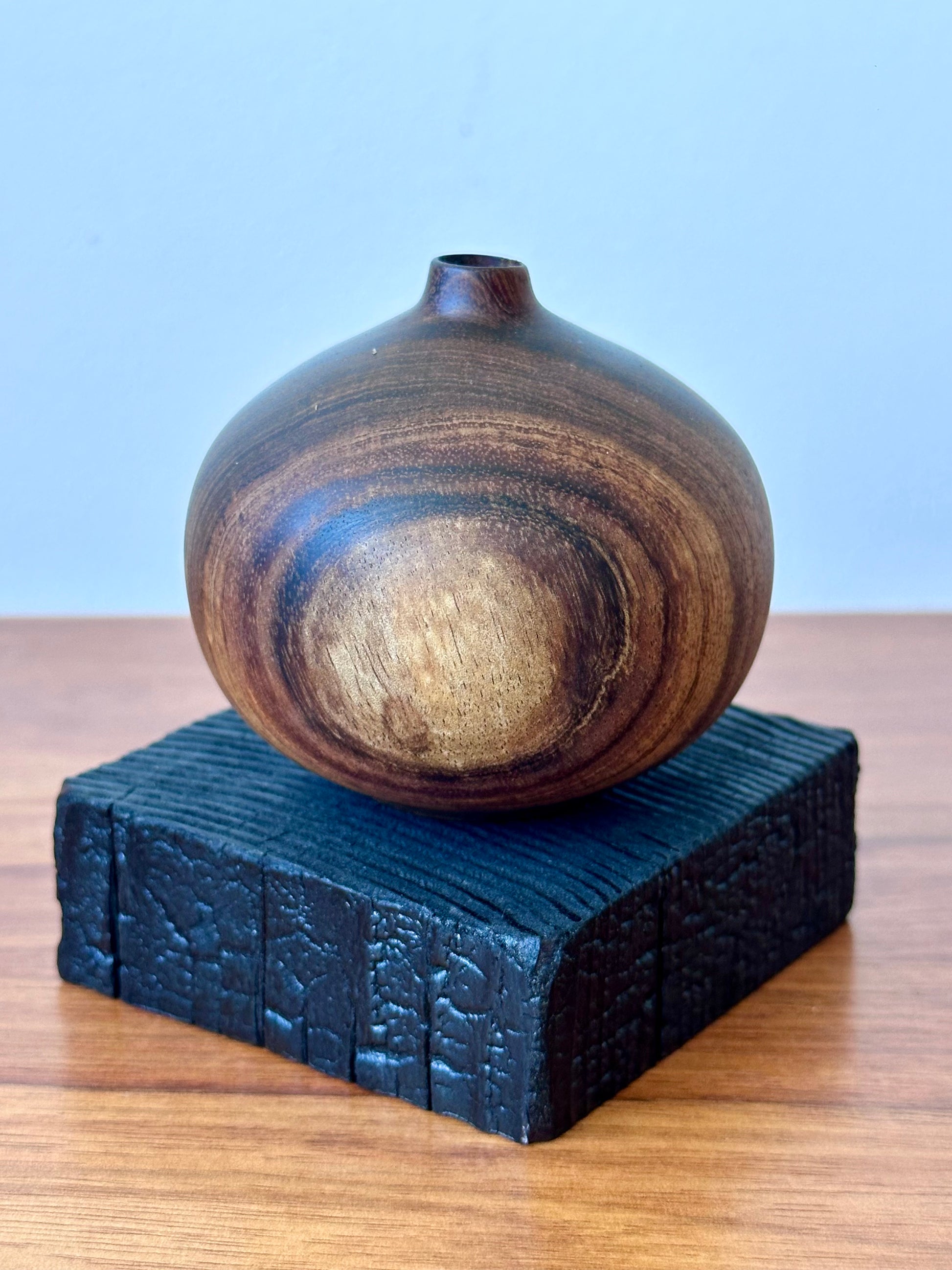 Wooden vase on a textured black stand against a light grey background